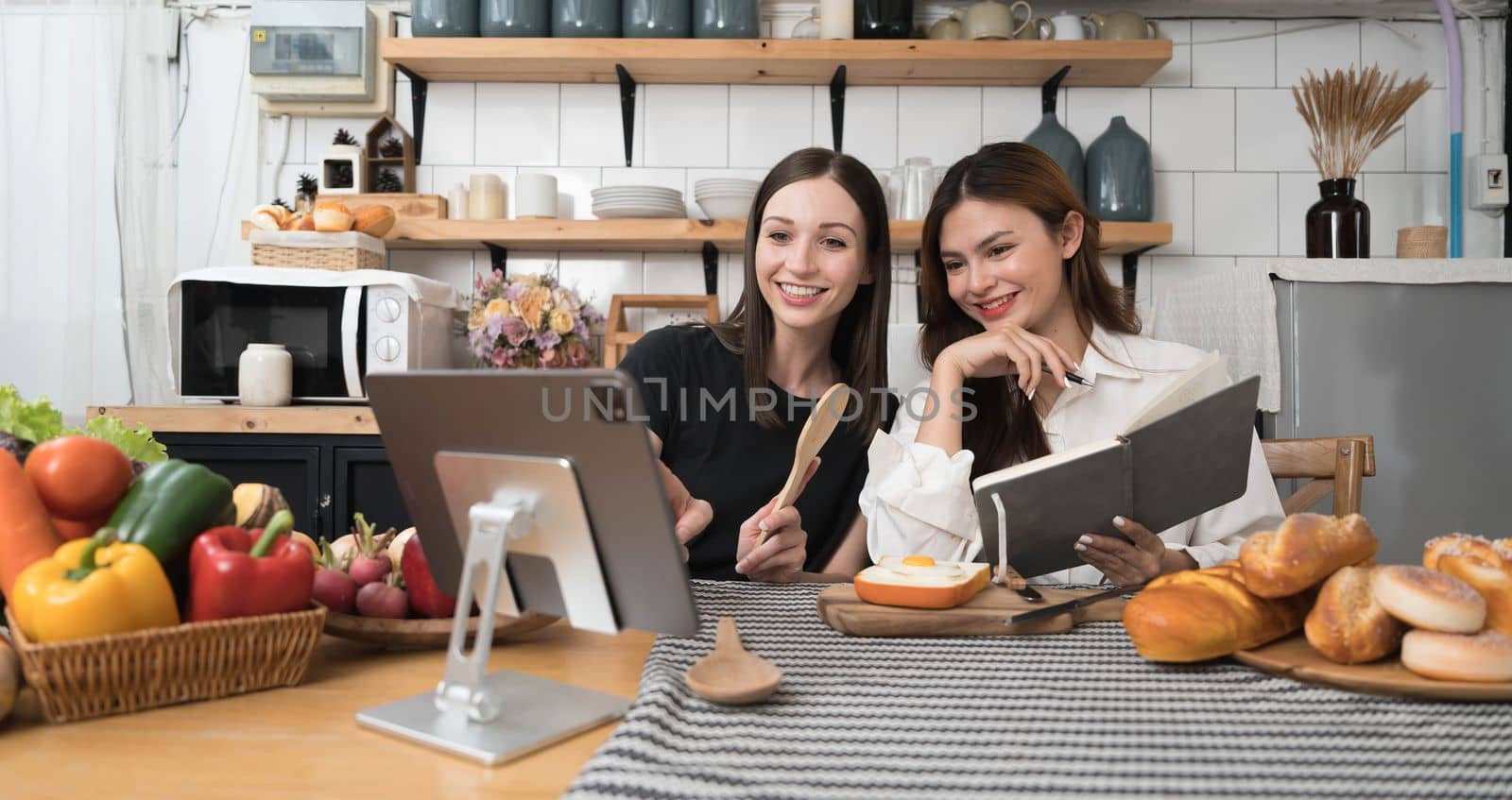 Female and female or LGBT couples are happily cooking bread together with happy smiling face in kitchen at home by wichayada