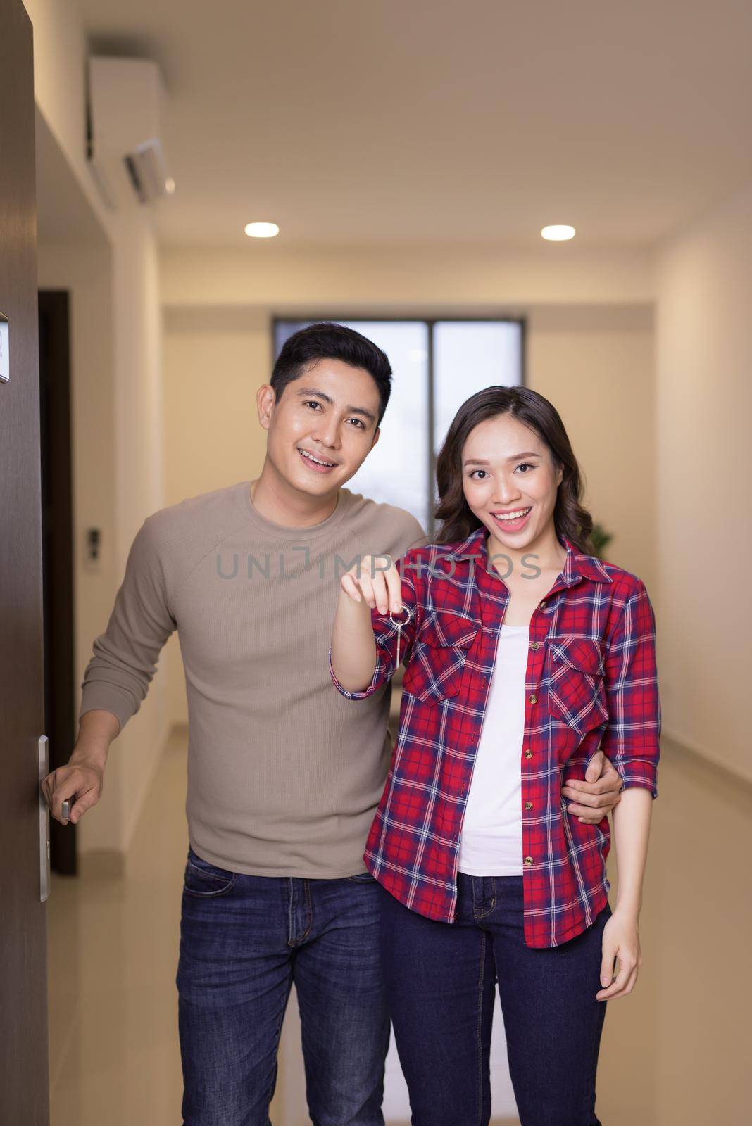Happy young couple handing their new home keys and open house door by makidotvn