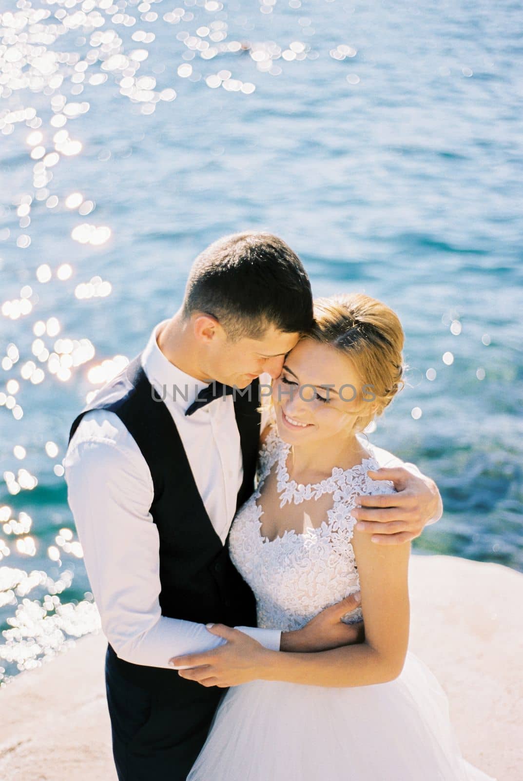 Groom hugs bride, leaning his forehead against her temple on the pier. High quality photo