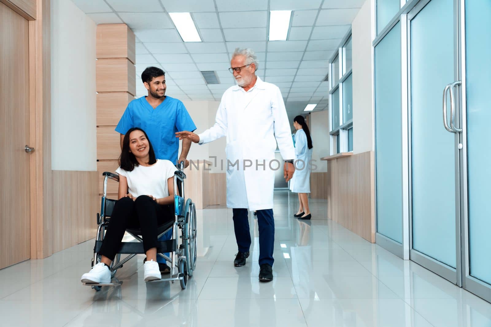 Doctor and nurse transport female patient in wheelchair at sterile corridor. by biancoblue