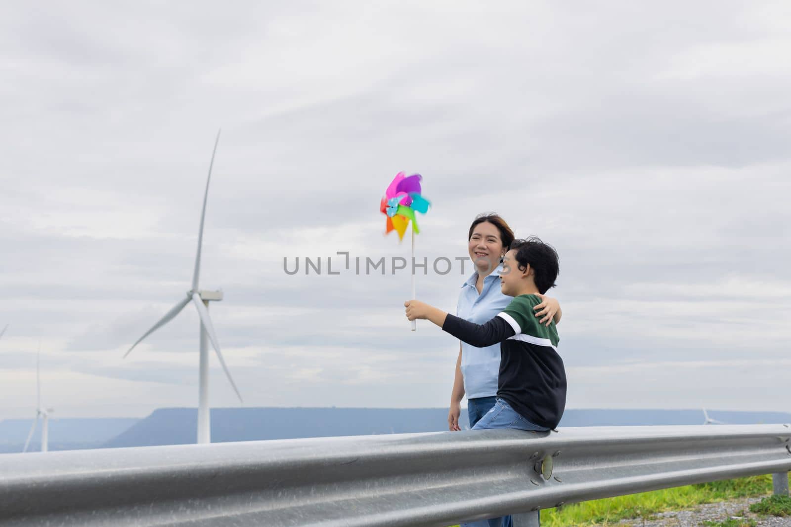 A progressive mother and her son are on vacation, enjoying the natural beauty of a lake at the bottom of a hill while the boy carries a toy windmill.