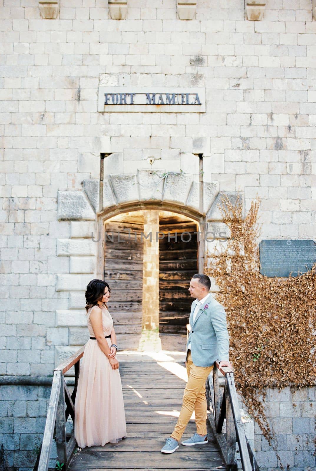 Bride and groom stand opposite each other on a wooden bridge to the entrance to Mamula Fort. High quality photo