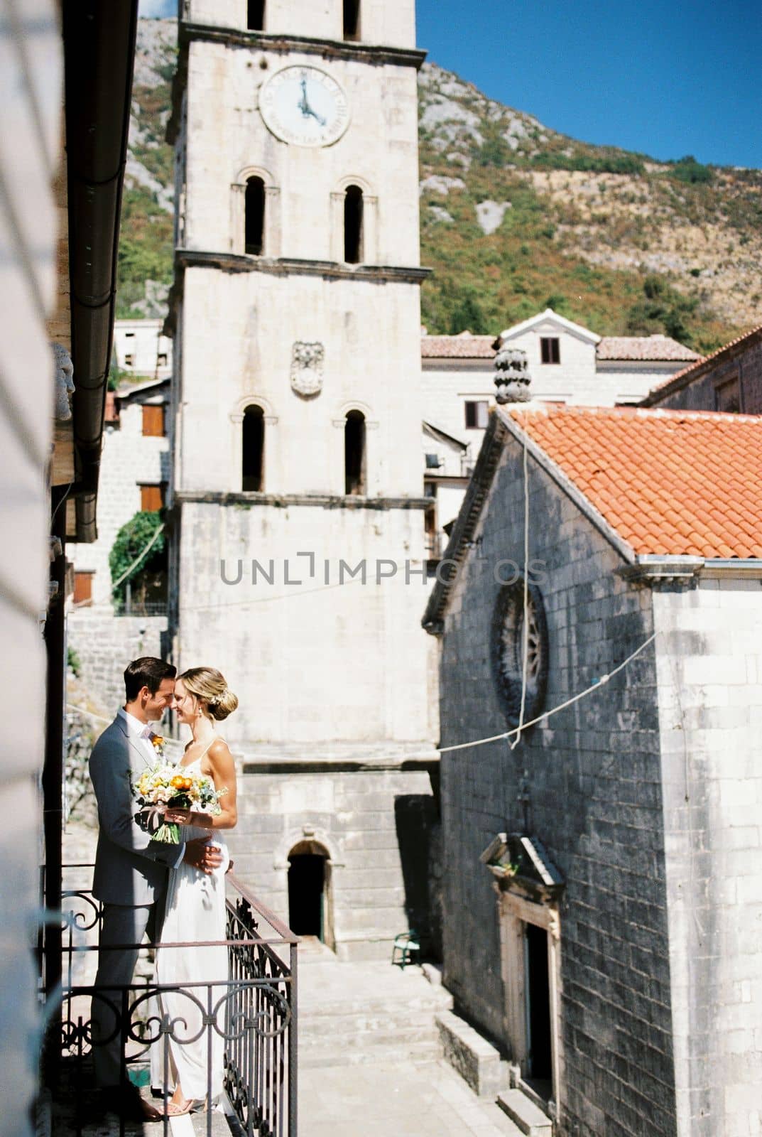 Groom hugs the smiling bride on the balcony near the ancient bell tower. High quality photo