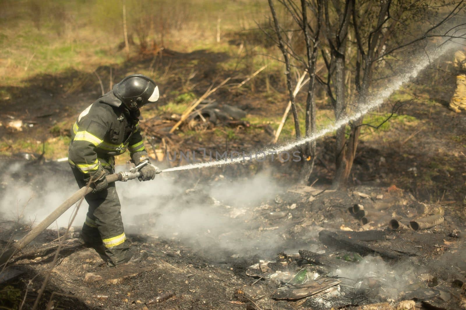 Firefighter puts out fire in woods. Lifeguard pours water. Fire in nature. Smoke and fire.