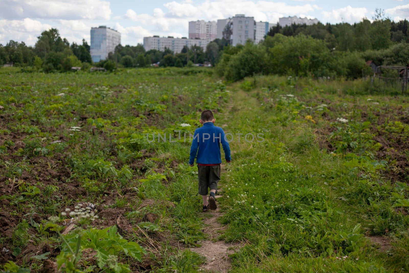 Child walks by nature. Schoolboy walks alone in summer. Boy in blue jacket on street. by OlegKopyov