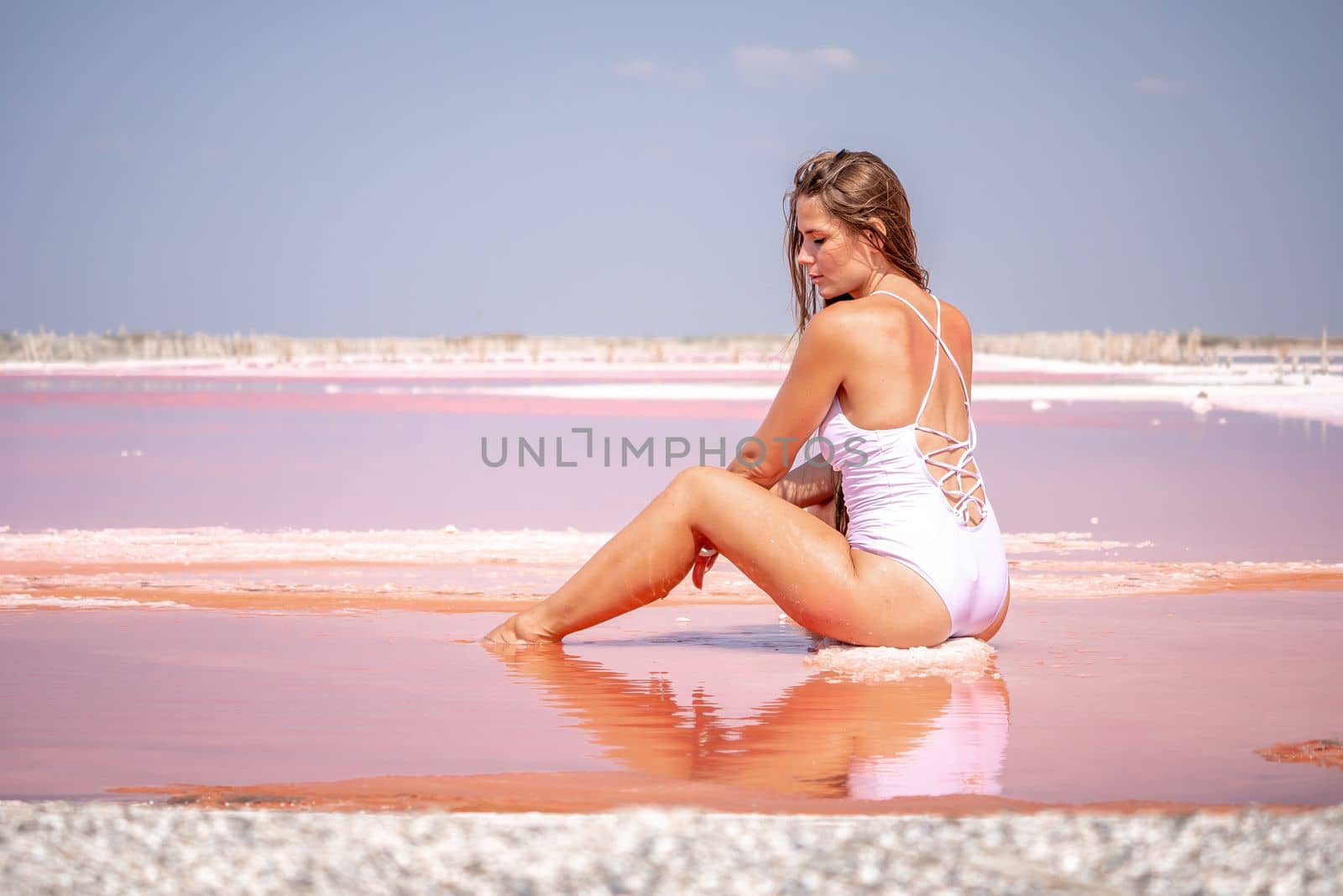 Young woman with long hair in pink salty lake with crystals of salt. Extremely salty pink lake, colored by microalgae with crystalline salt depositions. Spa, beauty and health care concept. by panophotograph