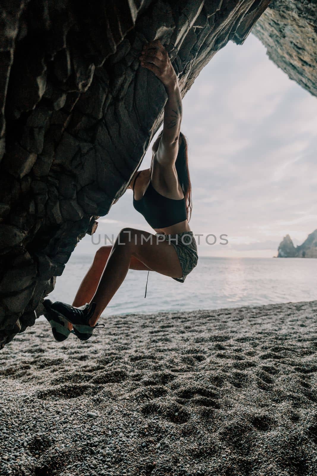 A girl climbs a rock. The athlete trains in nature. Woman overcomes difficult climbing route. Extreme hobby. Tourist woman rock climber hiking on mountains rocks over beautiful sea coast