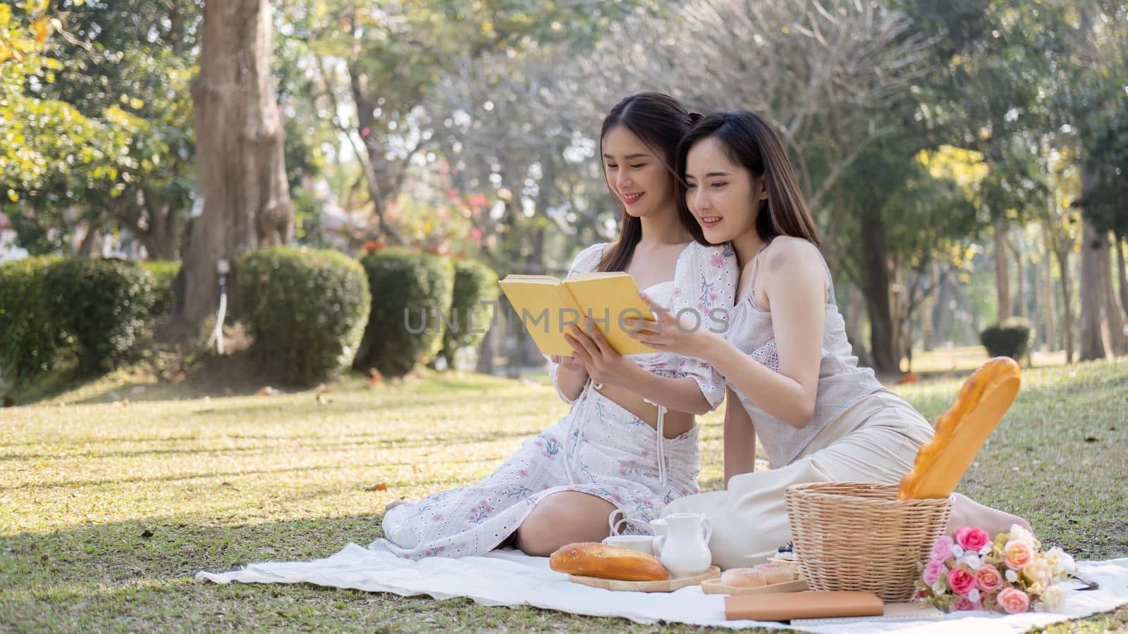 Two young Asian women beautiful read a book while picnicking in the beautiful garden together on the weekend.