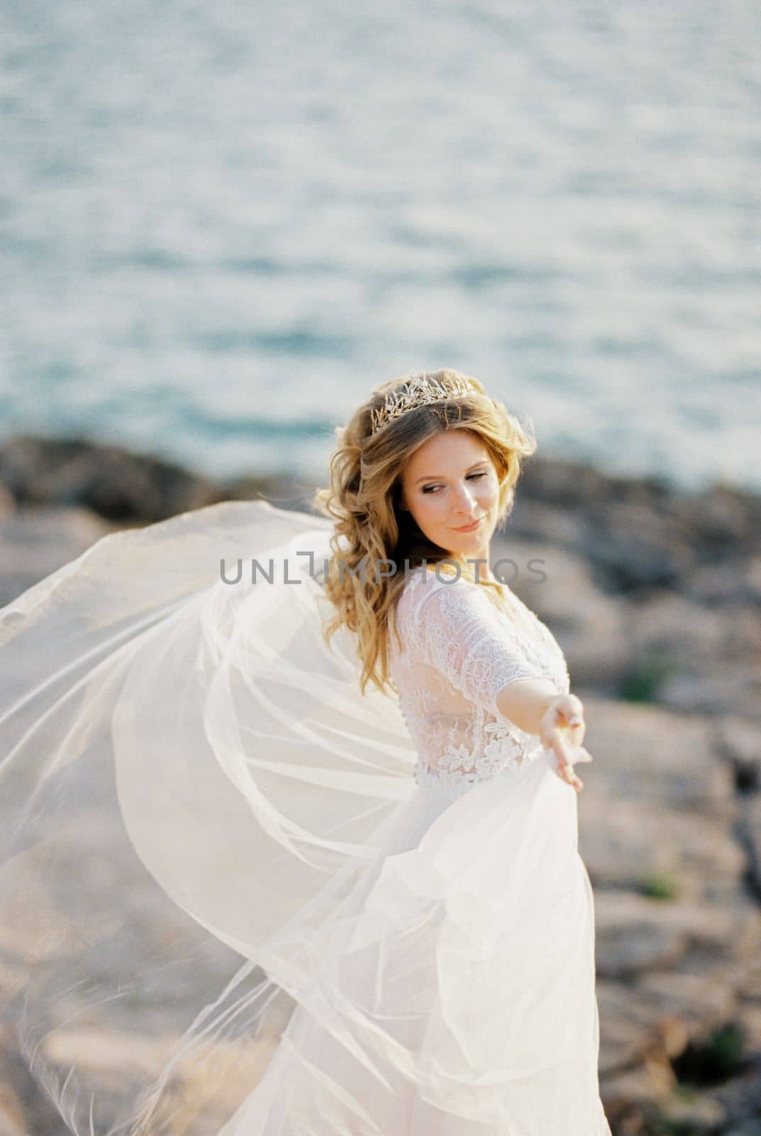 Bride in a dress fluttering in the wind stands on the stones with her arms outstretched. High quality photo