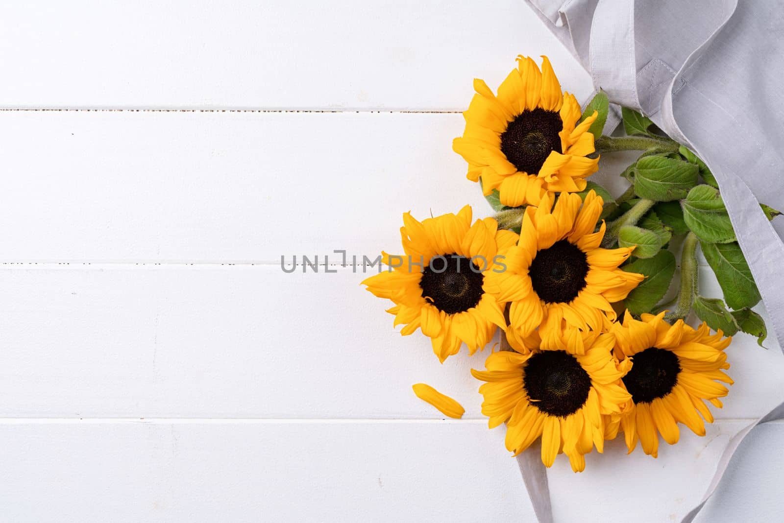 fresh sunflowers with leaves on stalk in shopping bag on wooden background. Flat lay, top view, copy space. by Desperada