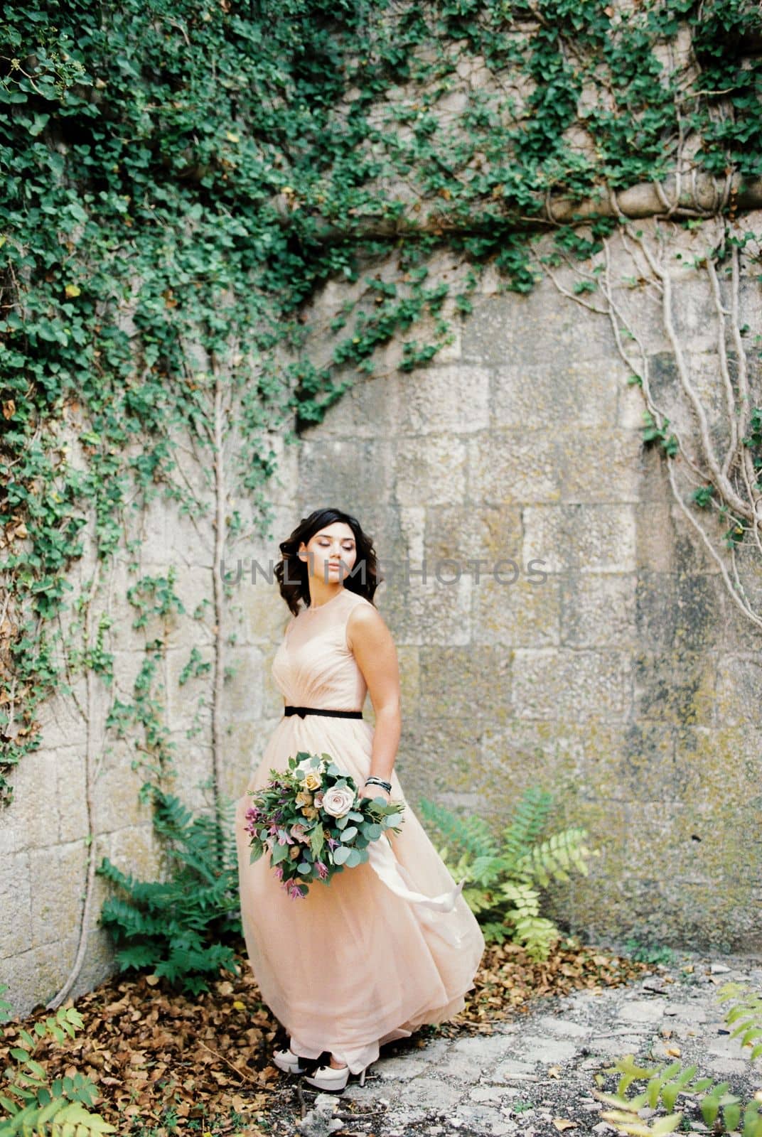 Bride stands in the corner of the courtyard of an ancient fortress overgrown with ivy. High quality photo