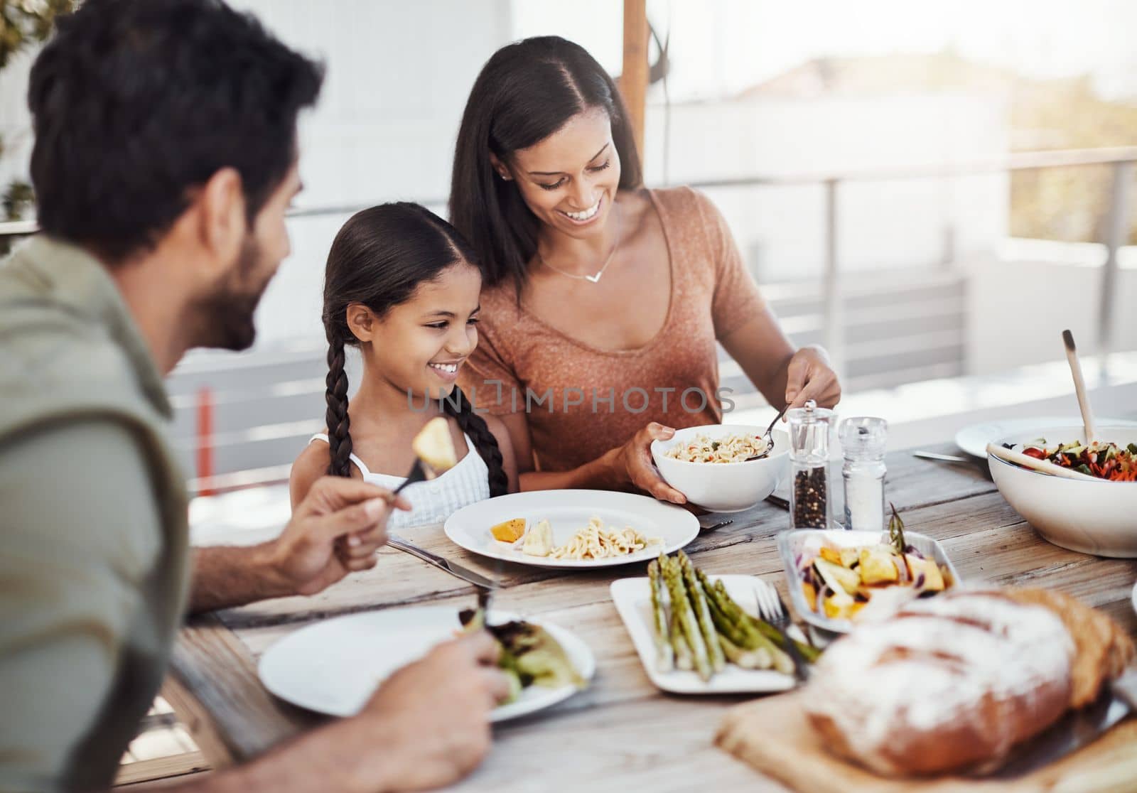 Making meal time, family time. a happy young family enjoying a meal together outdoors. by YuriArcurs