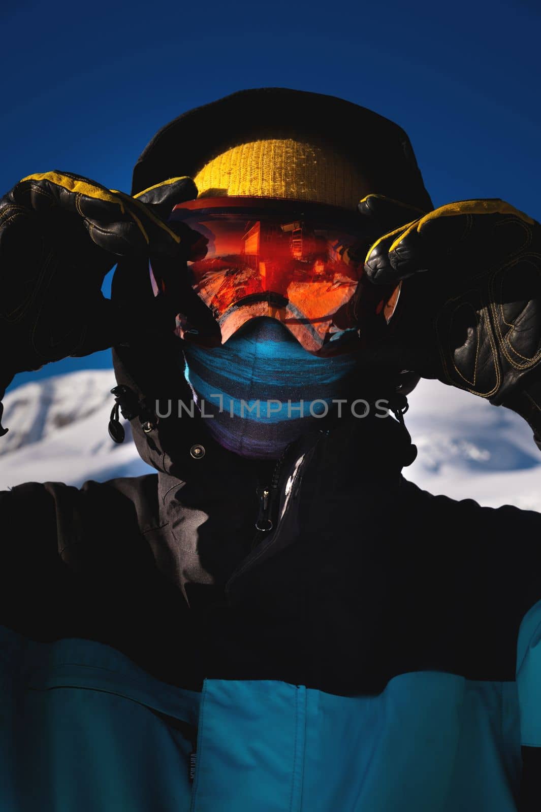 Close-up portrait of a skier in a mask with a closed face against the backdrop of snow capped mountains and blue sky on a bright sunny day by yanik88