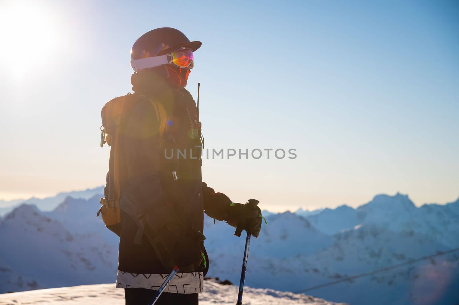 Side view of a snowboarder or skier against the backdrop of mountains at a ski resort in bright sunlight. Portrait of a rider with a backpack ready to go off-piste.