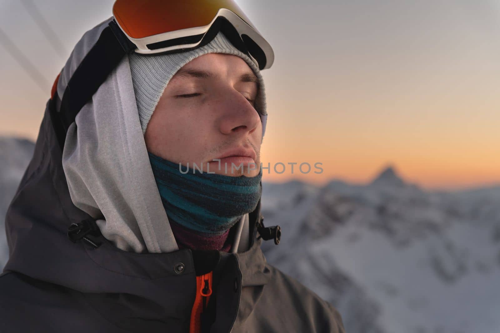 Close up portrait of happy young man in cold weather in winter mountains at sunset. The face of a peaceful man from the beauty of nature.