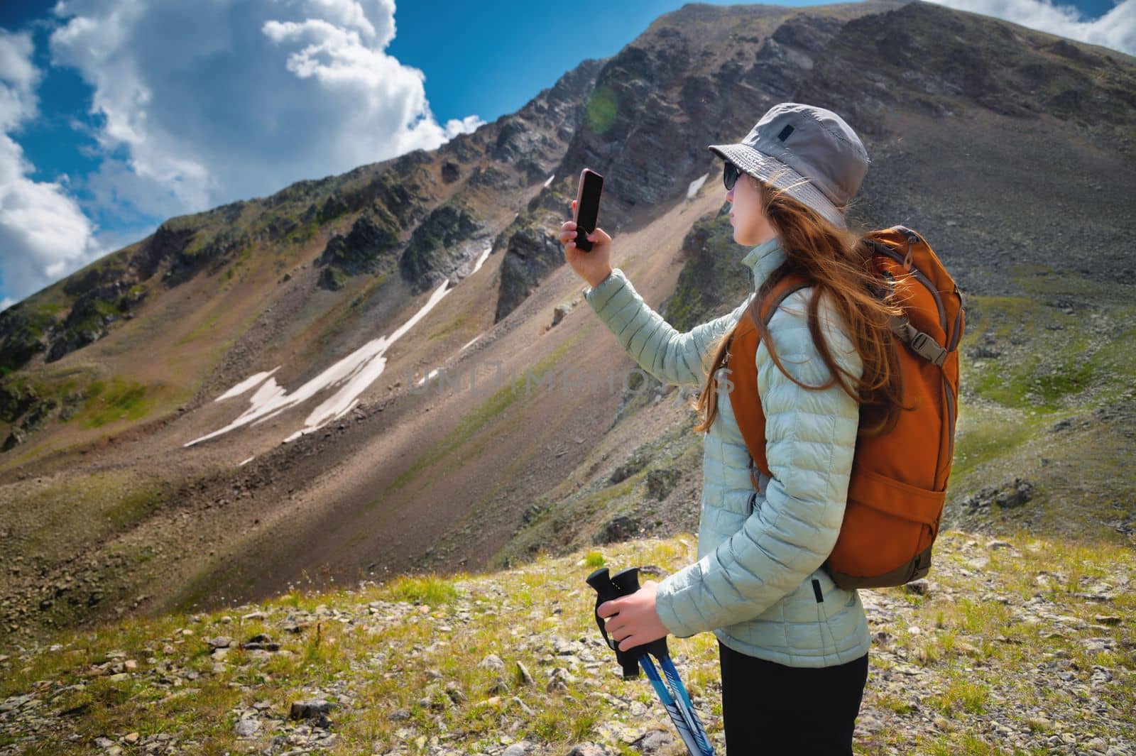 Side view of female blogger taking selfie on smartphone while hiking, discovering wild lands on vacation, wanderlust girl using phone to take photo while standing on rock, breathtaking scenery by yanik88