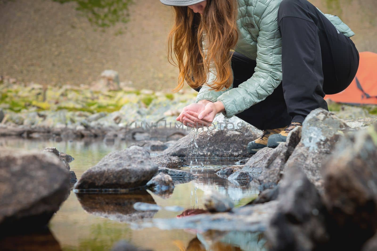 A young girl fills the palms of her hands with water from a stream of a cold mountain lake.