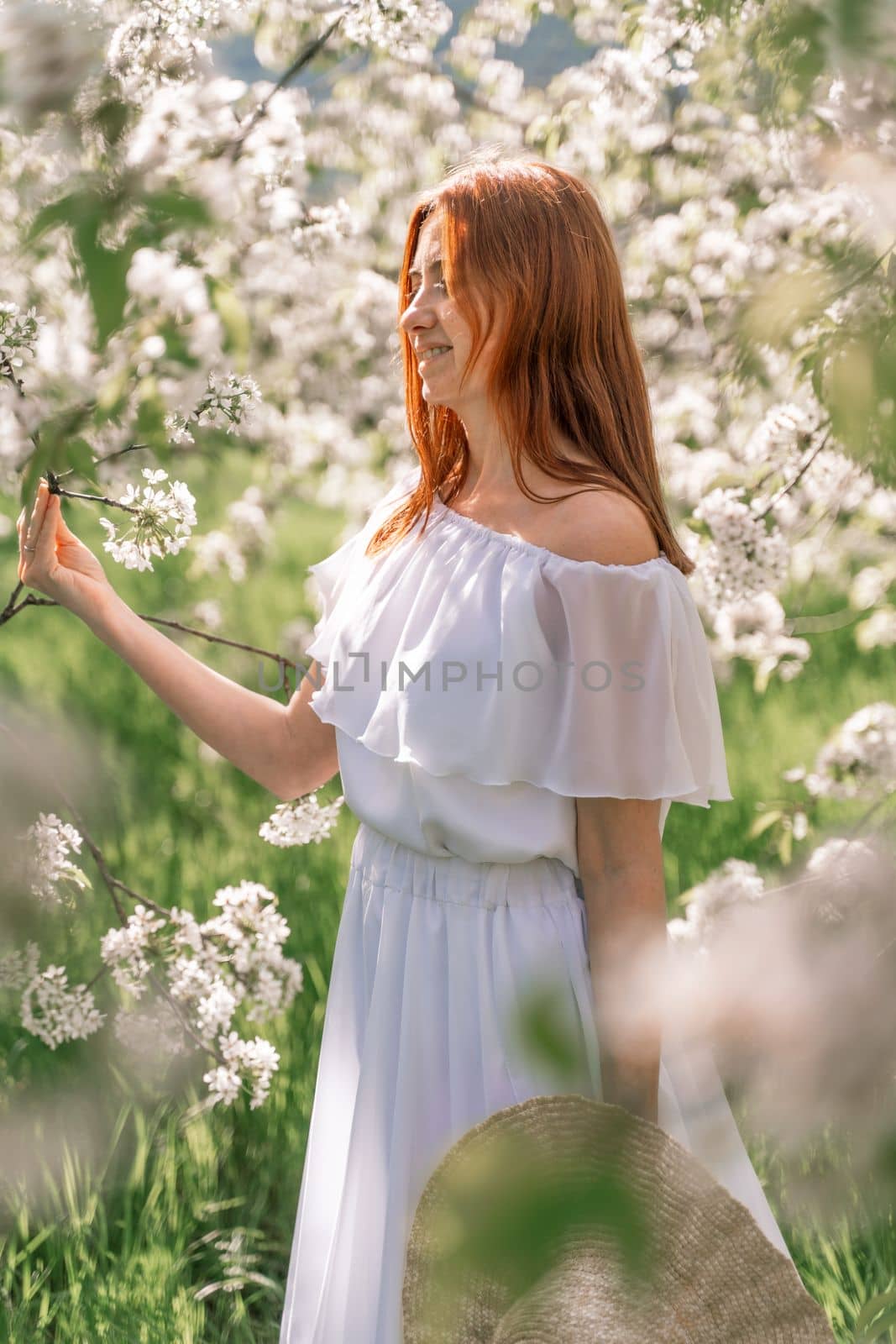 Woman cherry orchard. A happy woman in a long white long dress walks through the green spring blooming cherry garden. Happy cheerful princess bride. The fabric of the skirt flutters in the wind