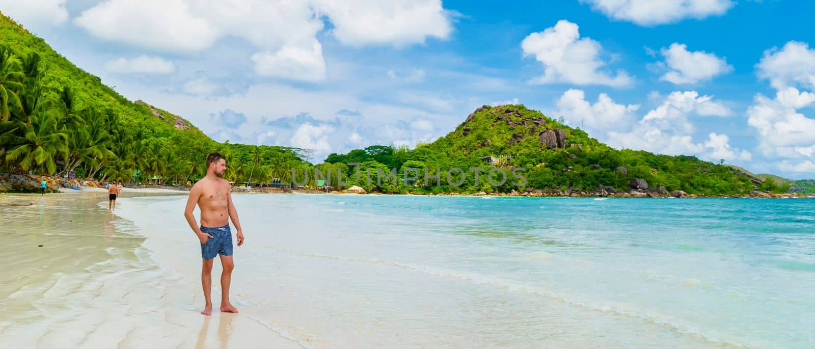 young man in swim short at a white tropical beach Anse Volbert beach Praslin Seychelles by fokkebok