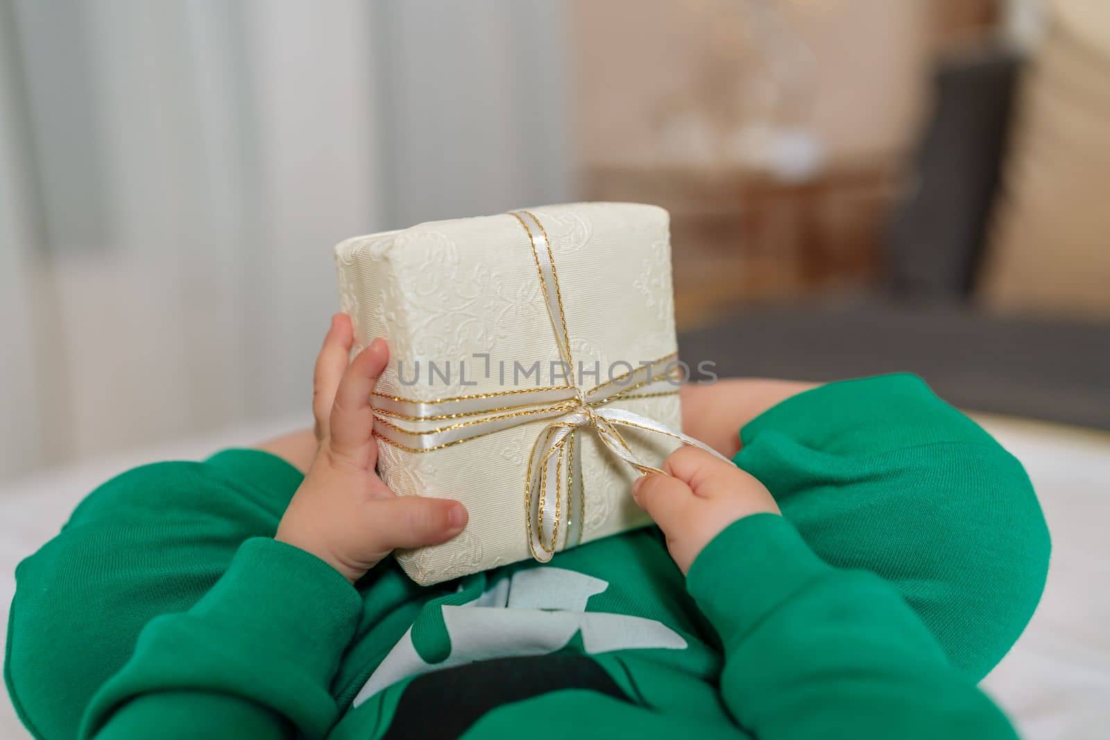 Kid gift. A little boy in a green suit holds a gift box with his feet and hands in bed