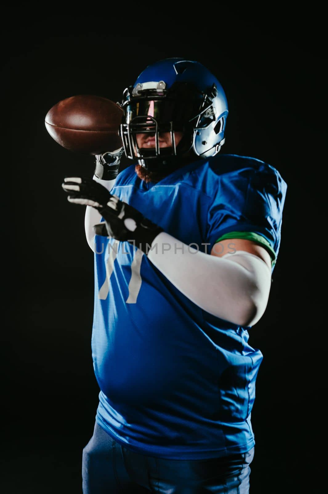 An Asian man with a red beard in a blue American football uniform throws a ball against a black background. by mrwed54
