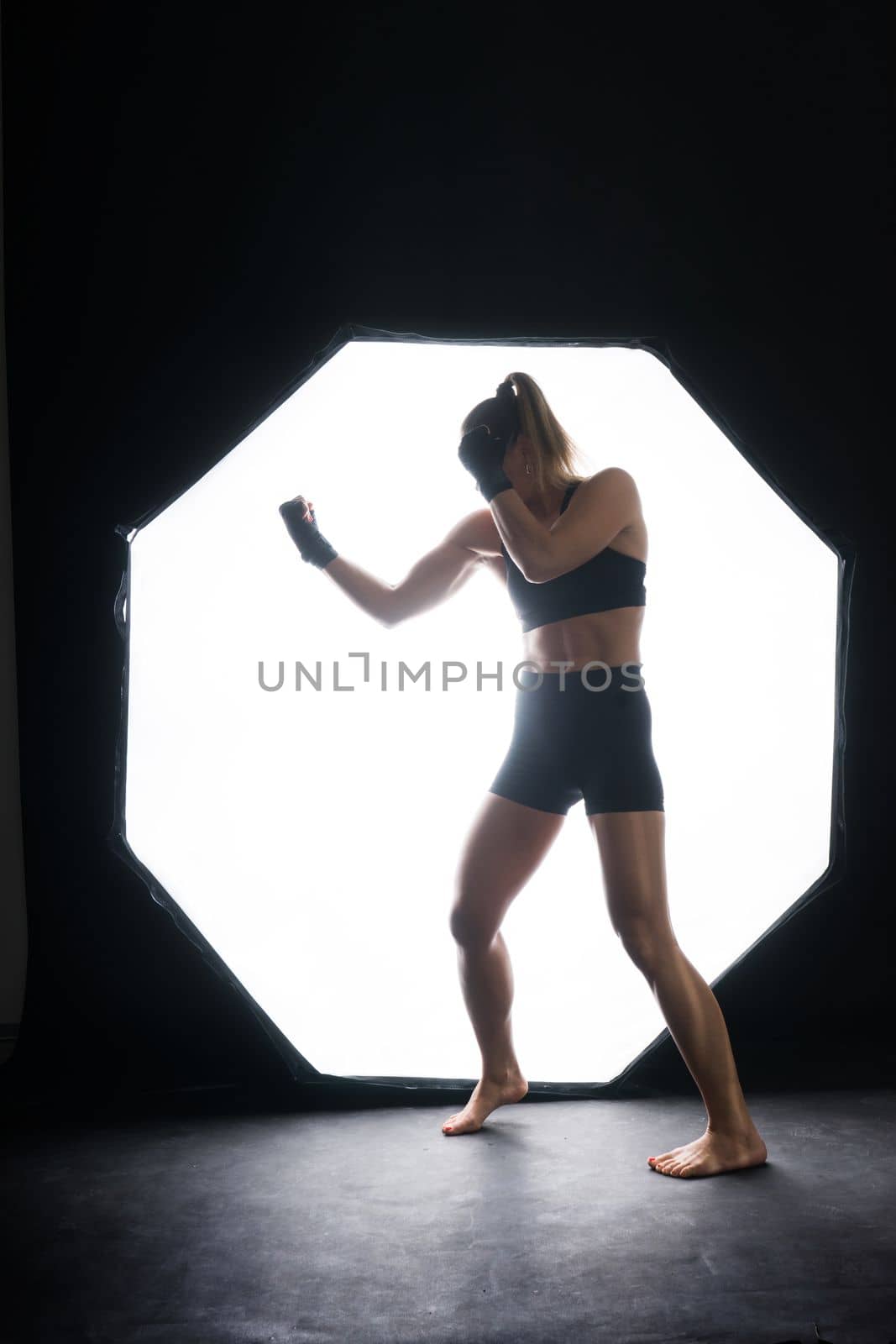 Cool female fighter in boxing bandages trains in a studio. Mixed martial arts.