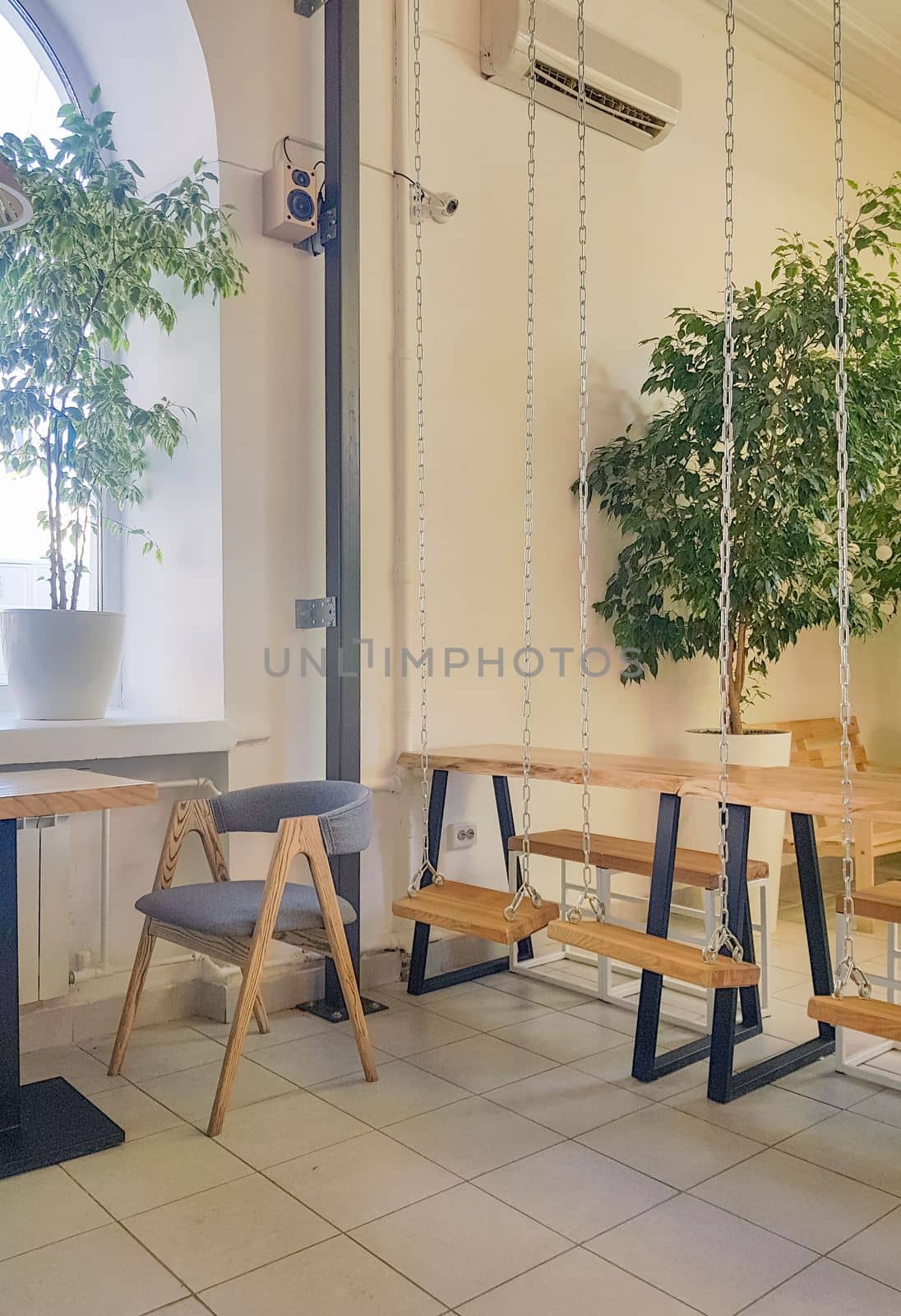 Cozy interior of a modern cafe in vintage style, with wooden tables and swings on chains. vertical photo.