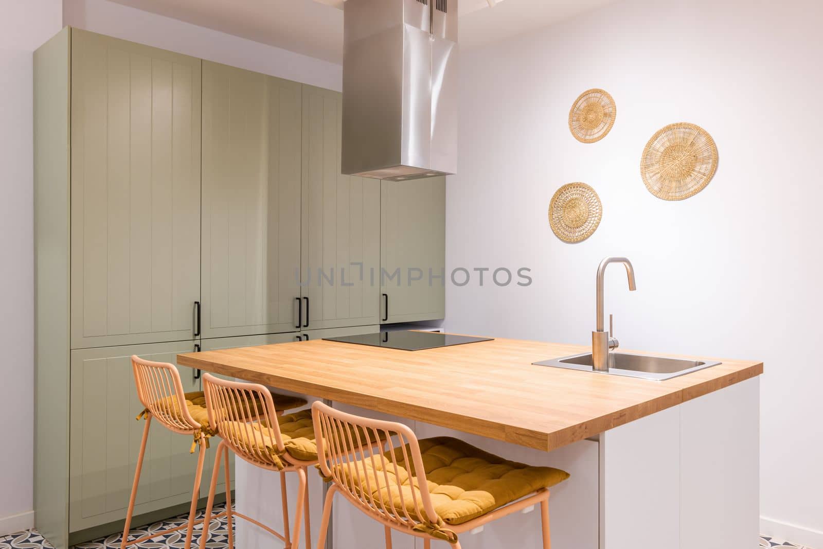 Closeup of kitchen table with trendy design high chairs. Wooden top and chairs in single honey color palette. Countertop has built-in sink and ceramic plate above which exhaust system is located