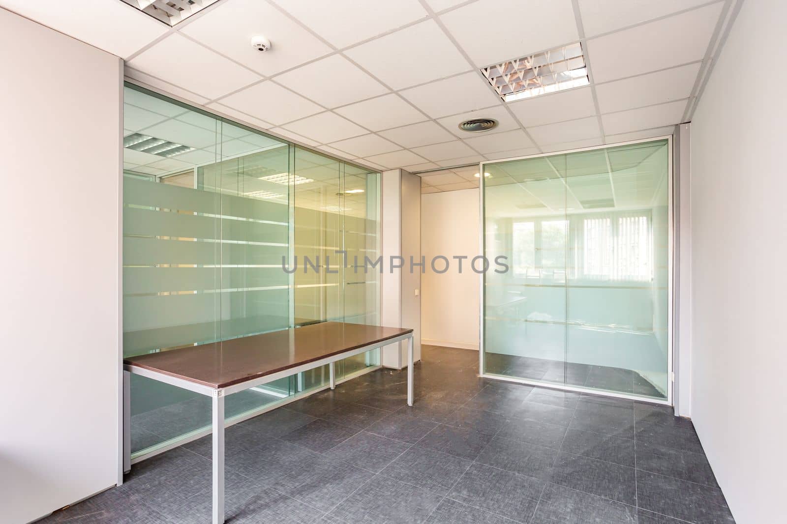 In a bankrupt office building, one of the many empty rooms with transparent, solid glass wall panels and an outdated ceiling covering is in need of repair and refurbishment. by apavlin