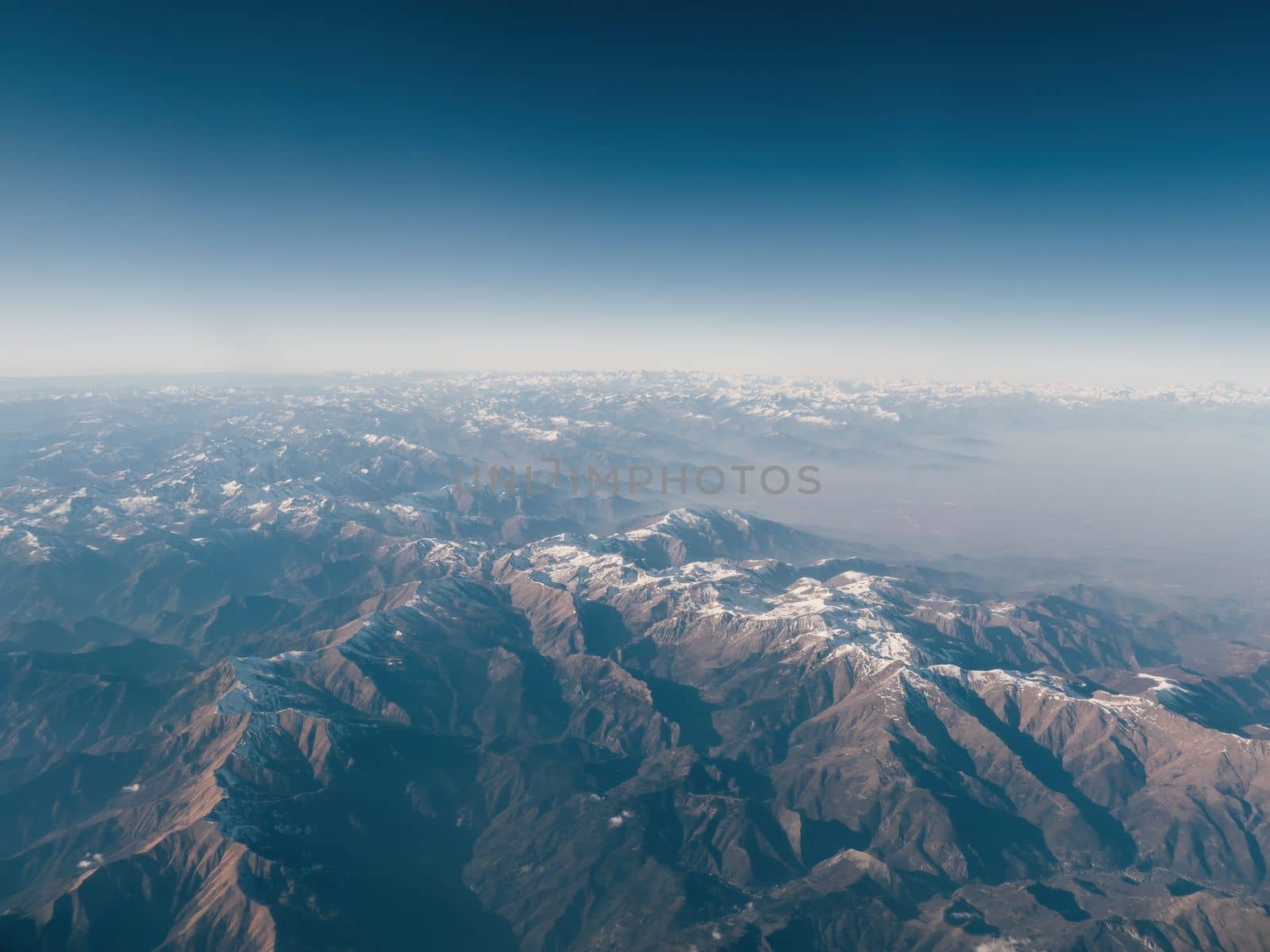 Amazingly beautiful panoramic aerial view of snow-capped mountain ranges of Alps. Flight over Alpine mountain peaks covered with snow in places. Mountain range to horizon with azure sky. by apavlin