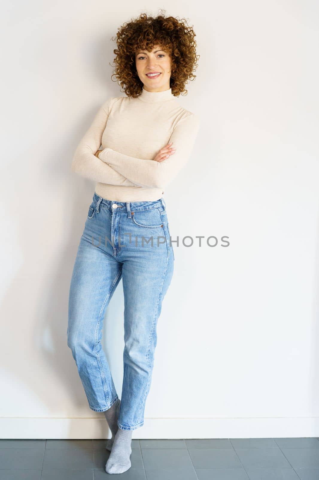 Confident woman standing against white wall crossing arms by javiindy