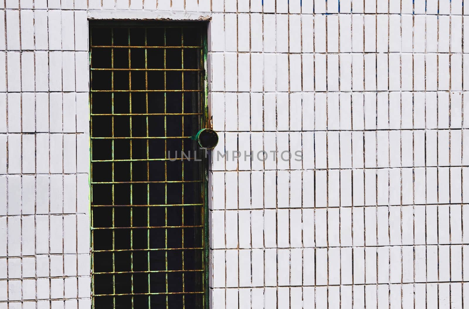 a hinged, sliding, or revolving barrier at the entrance to a building, room, or vehicle, or in the framework of a cupboard. Dark metal door hole with bars on a white tiled wall