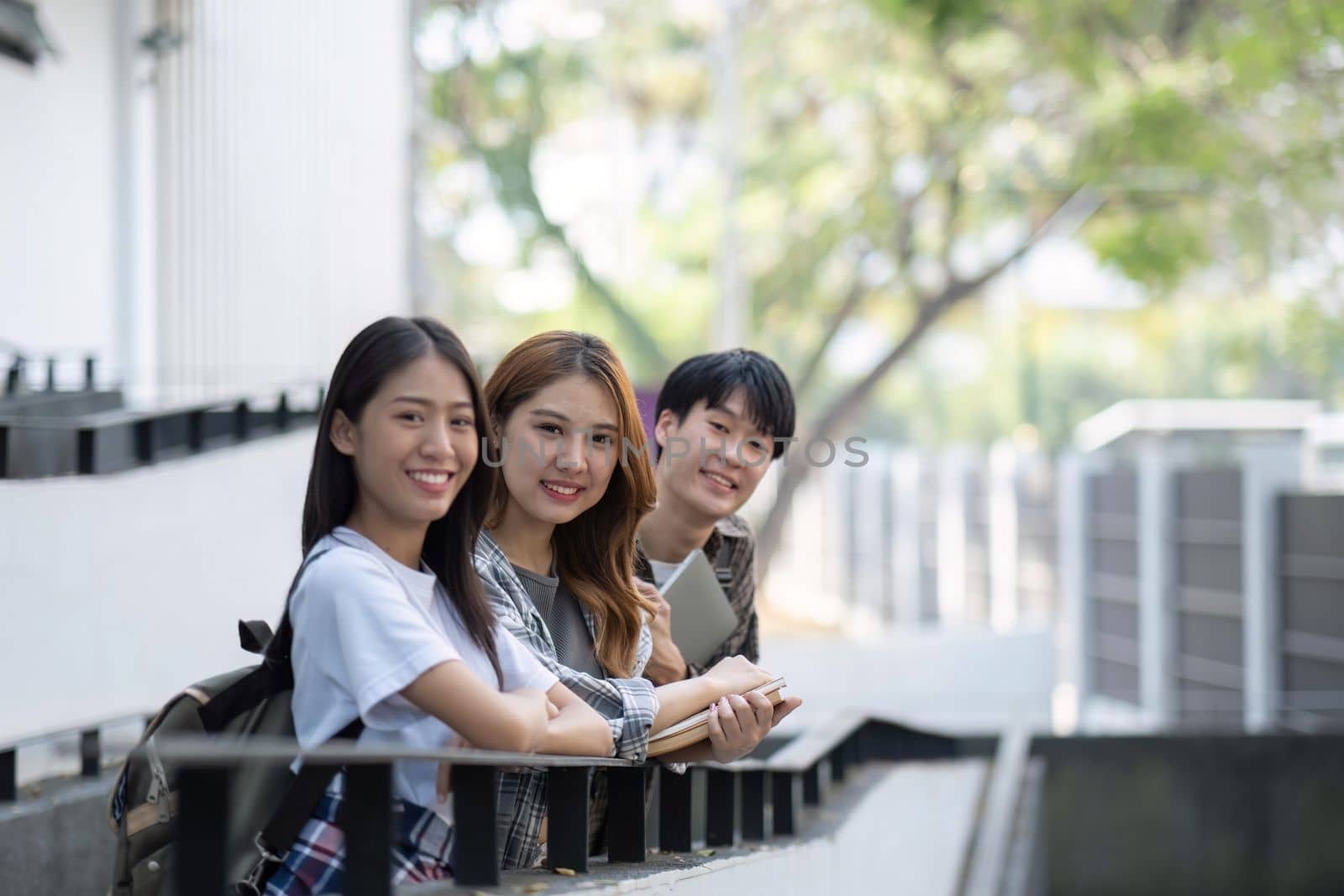 Group of young Asian college students sitting on in front of the school building, talking and focusing on their school project.