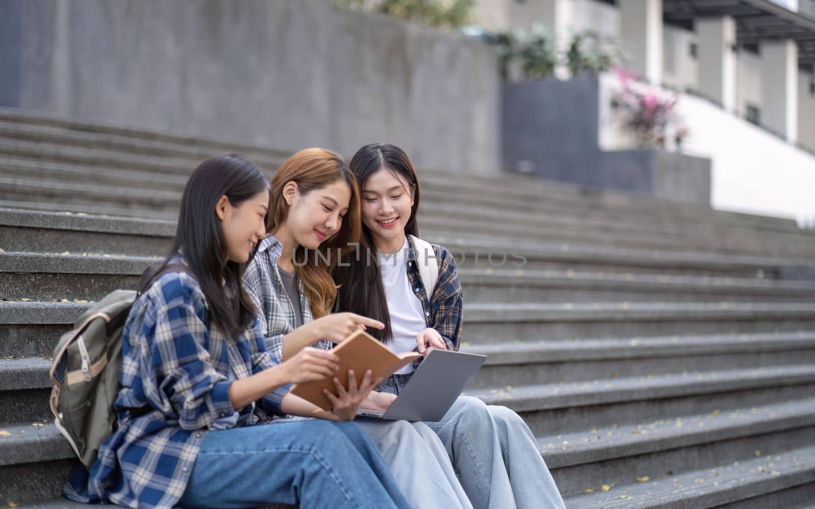 Nice young students use laptop after class sitting outdoors. girls wear casual clothes in spring. Concept of modern education by nateemee