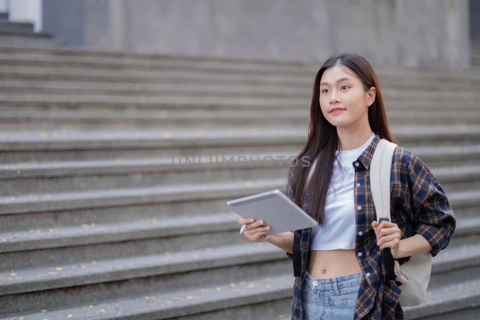 Asian female college student with her laptop in front of the campus building.