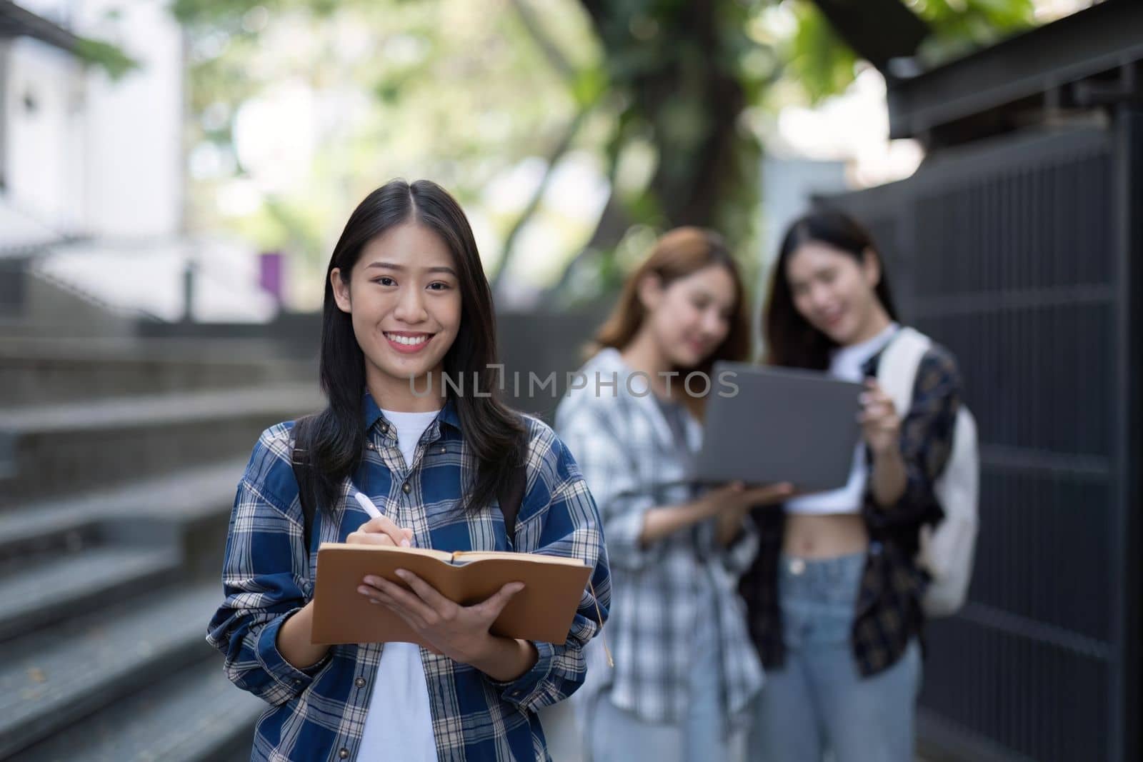 Asian female college student with her school book stands in front of the campus building.