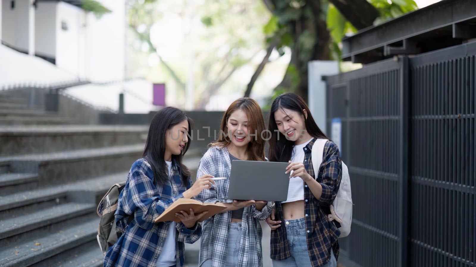 Nice young students use laptop after class sitting outdoors. girls wear casual clothes in spring. Concept of modern education.