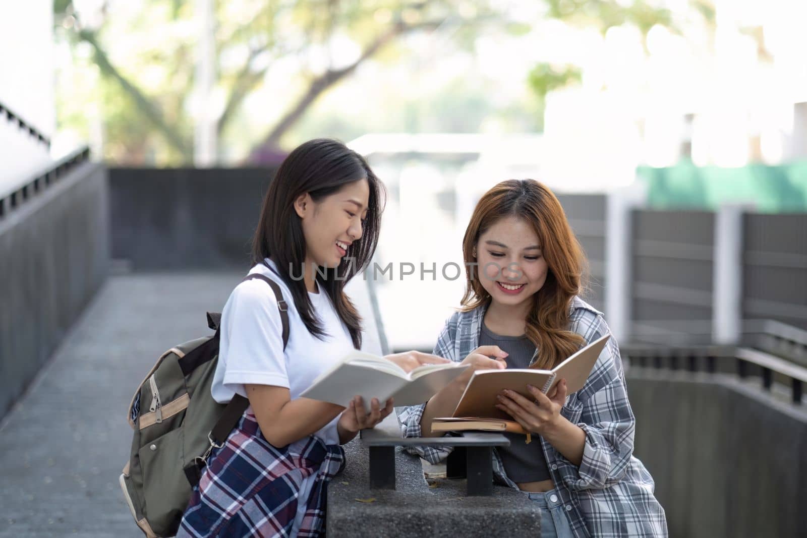 Cheerful Asian college two female students are talking, sharing ideas, working on their school project together by nateemee