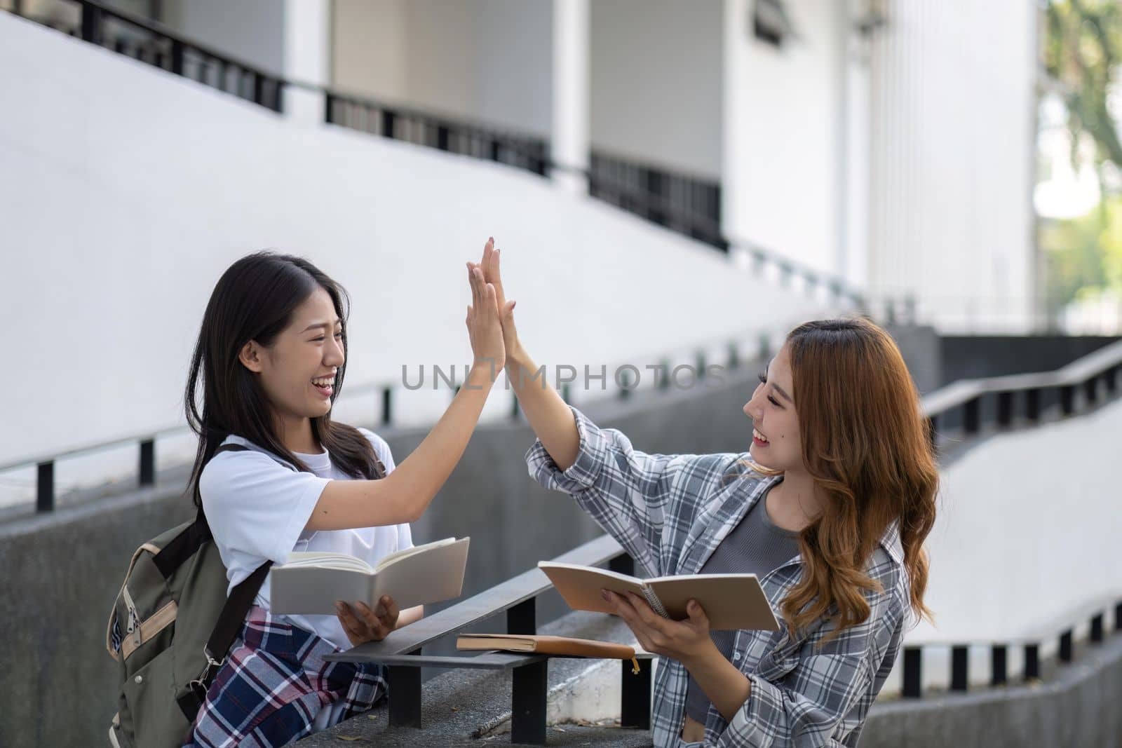 Cheerful Asian college two female students are talking, sharing ideas, working on their school project together.