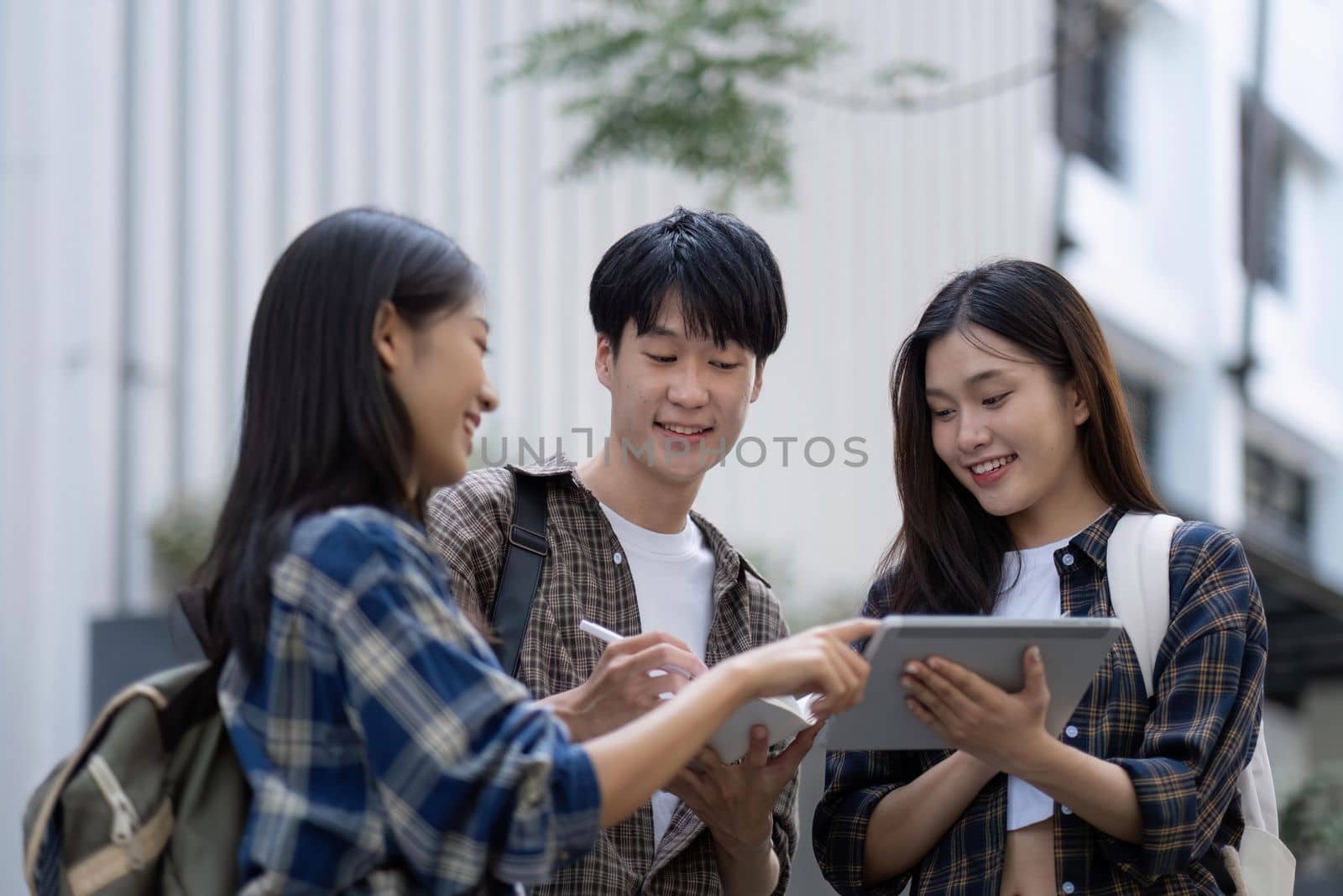 Group of young Asian college students sitting on in front of the school building, talking and focusing on their school project.