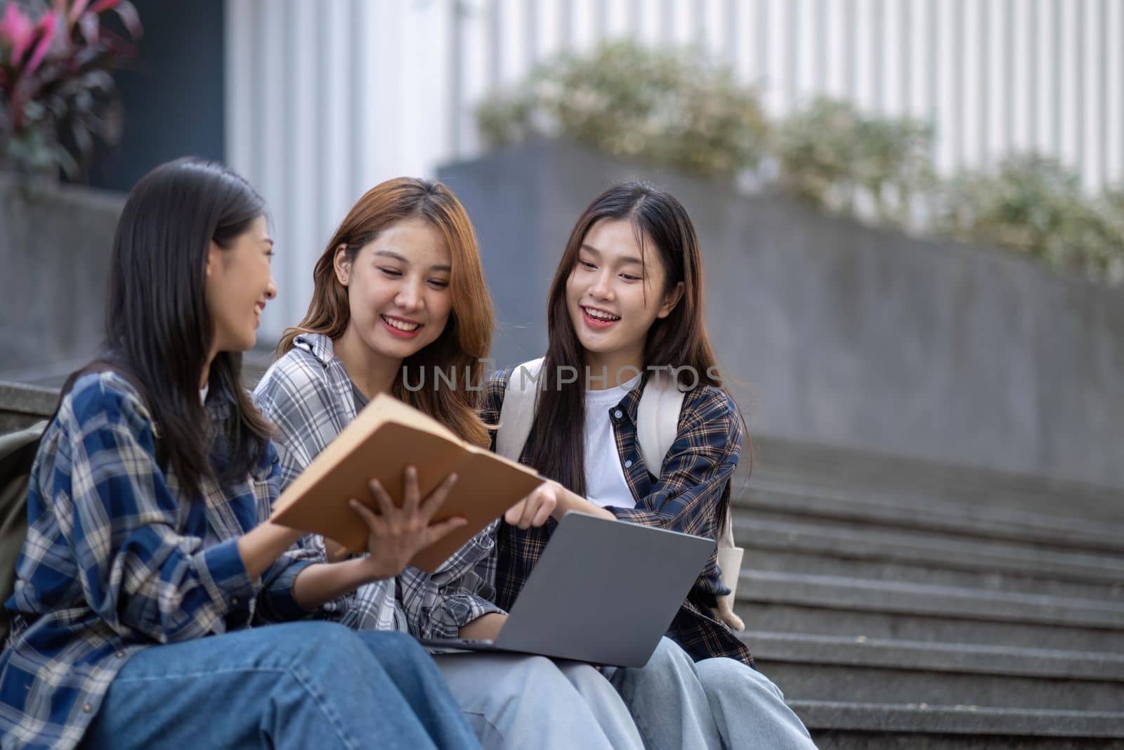 Nice young students use laptop after class sitting outdoors. girls wear casual clothes in spring. Concept of modern education.