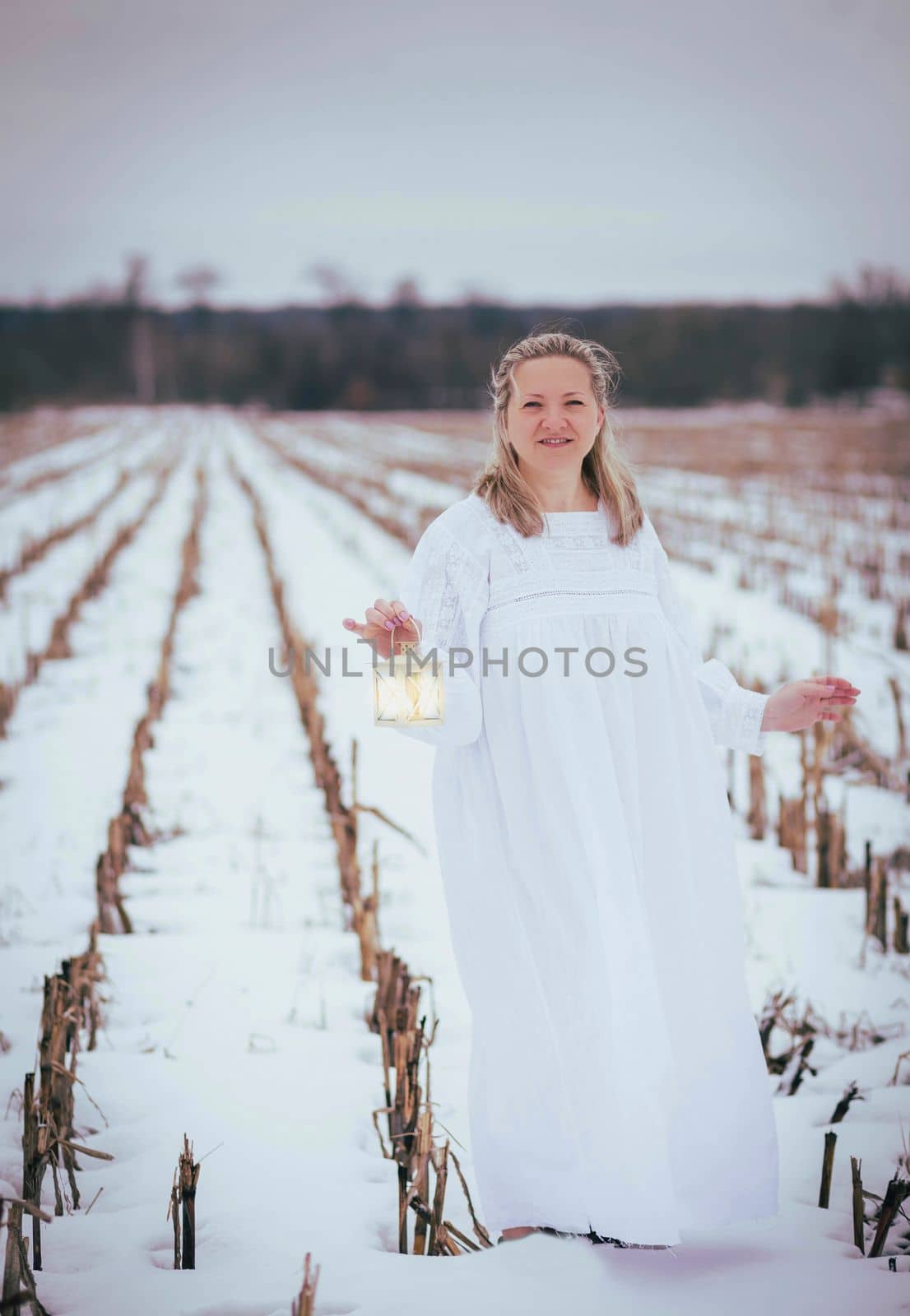 Attractive woman in nightgown in the field in winter with hand lamp.