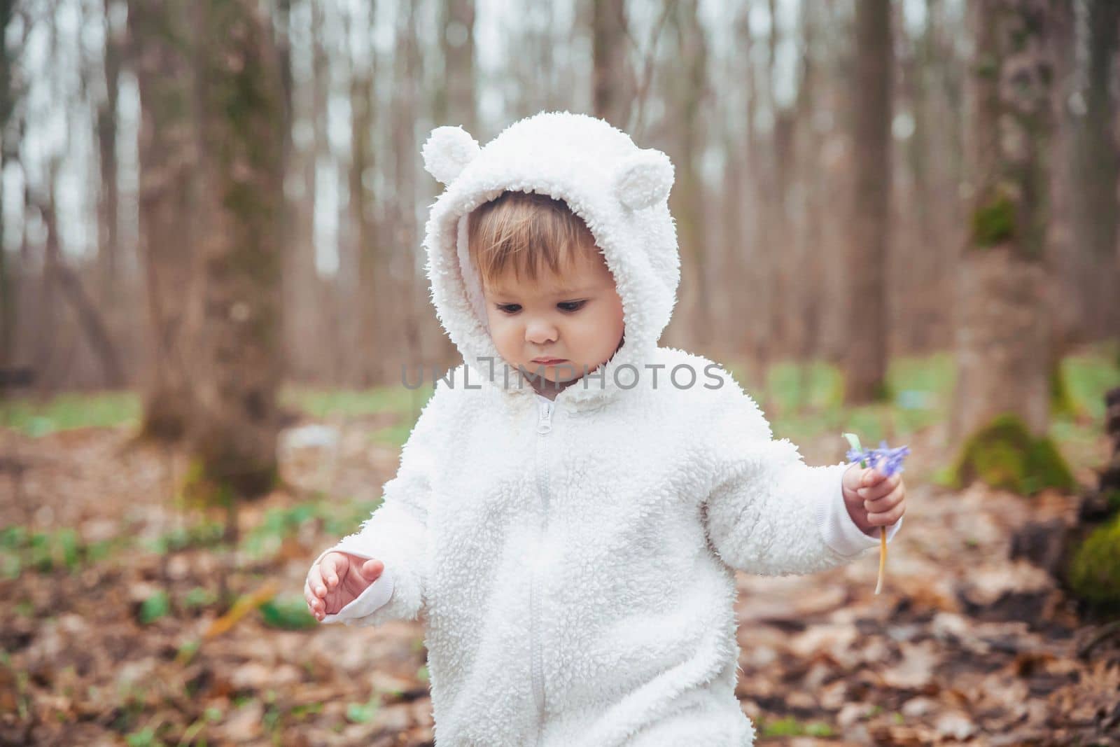 Adorable baby in a bear costume in the forest by a fallen tree.