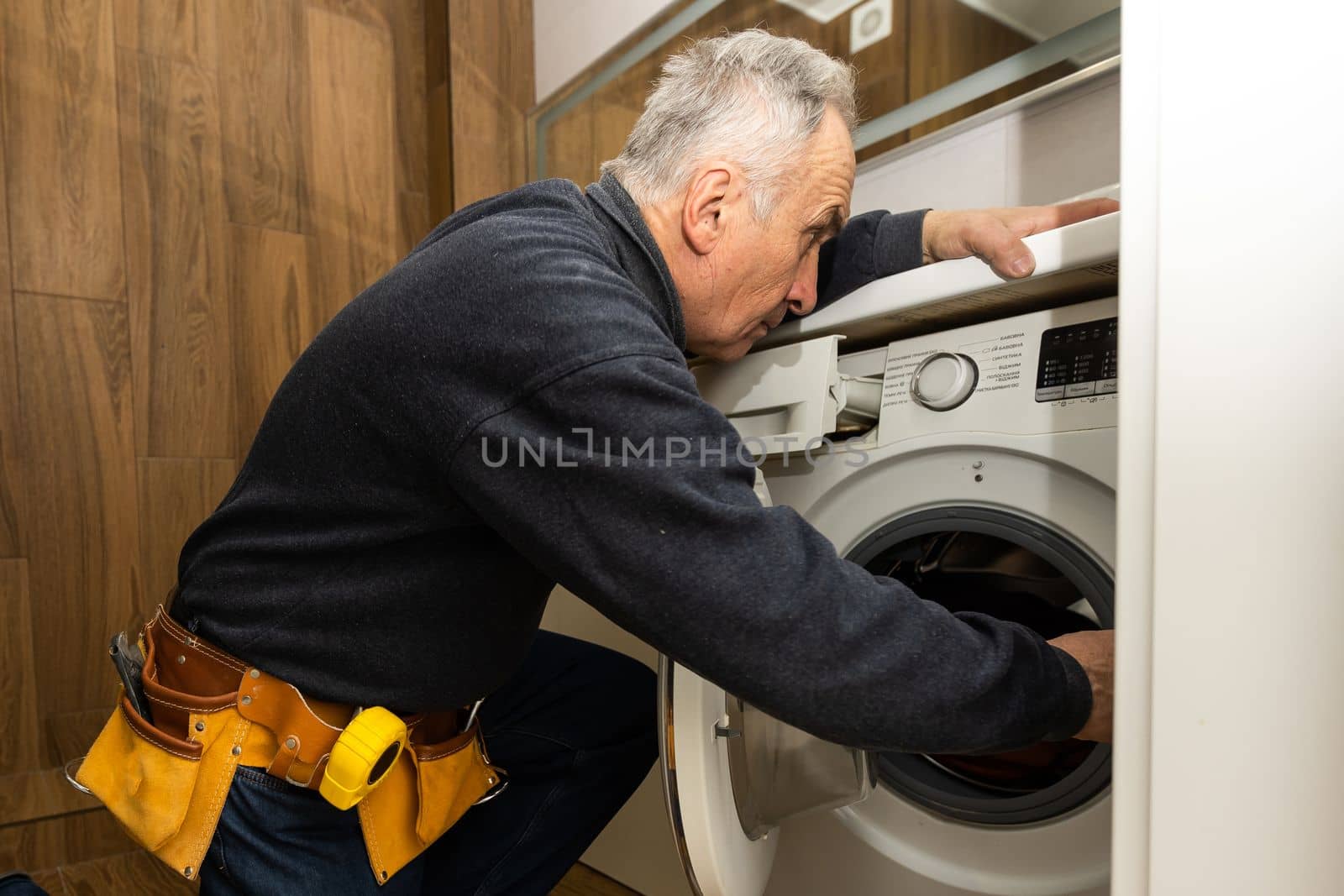 an elderly man repairs a washing machine.