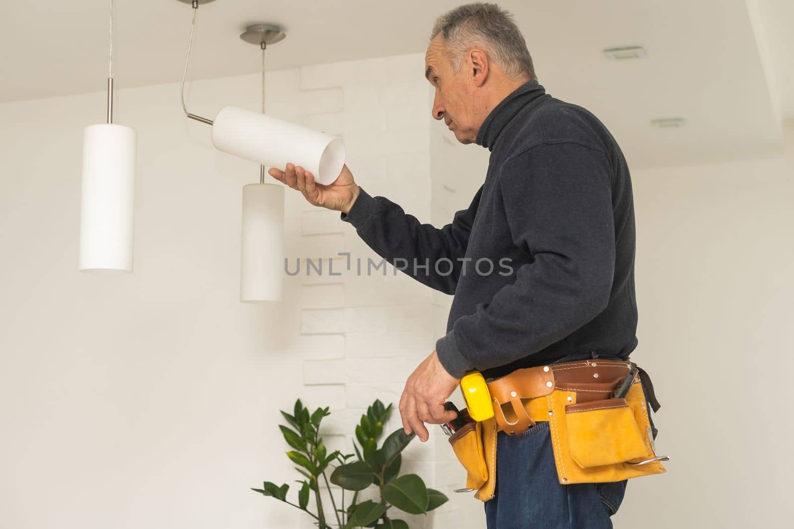 A male electrician changes the light bulbs in the ceiling light. men's household duties. care of electrical appliances at home by Andelov13