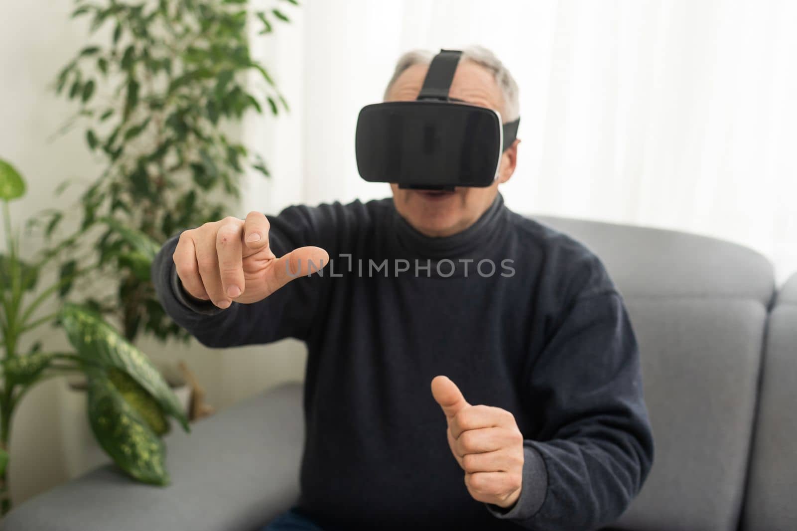 handsome senior man using VR 360 glasses at home. Making browse and tap gestures. Concept of active modern elderly people, learning to use contemporary technologies