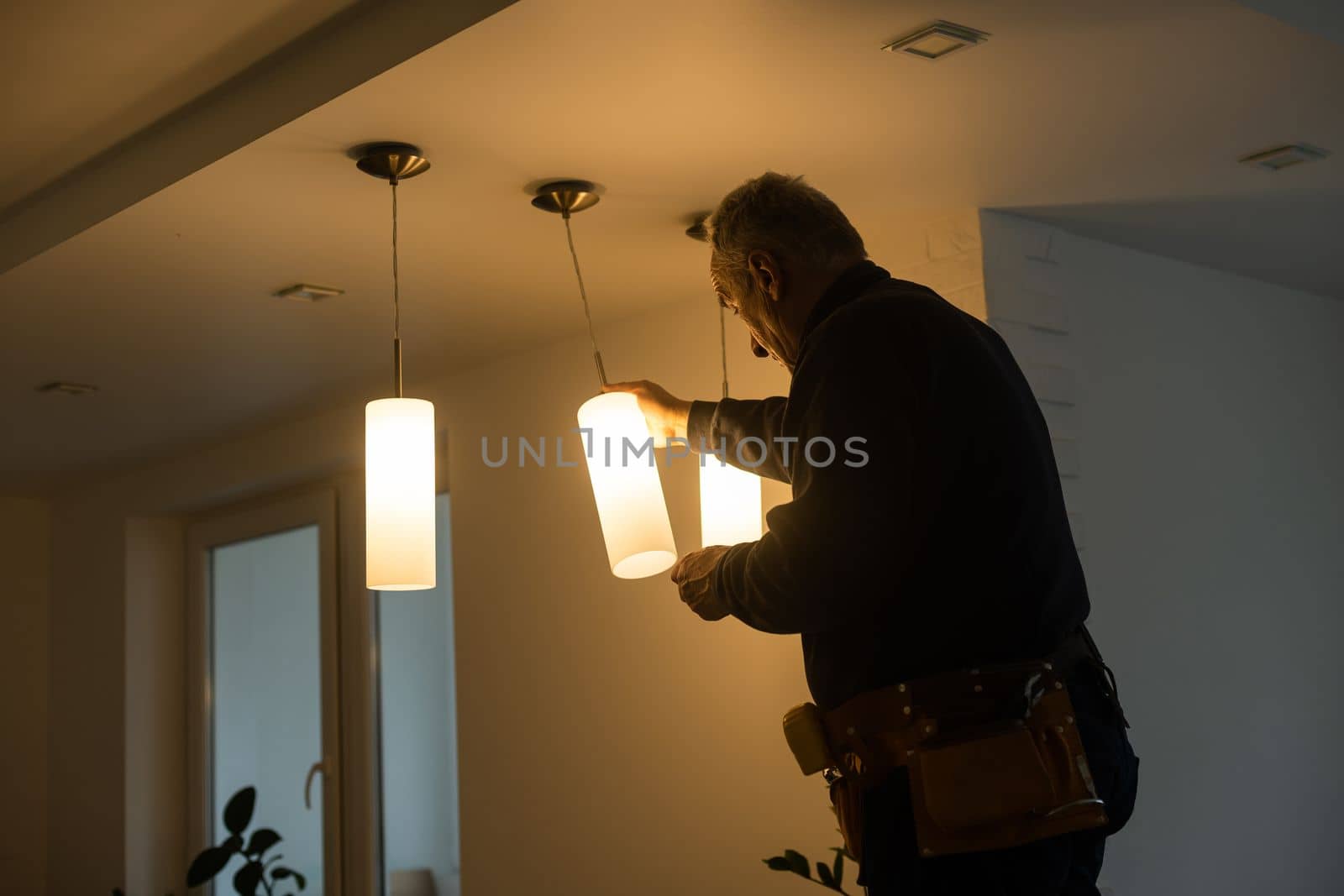 A male electrician changes the light bulbs in the ceiling light. men's household duties. care of electrical appliances at home by Andelov13