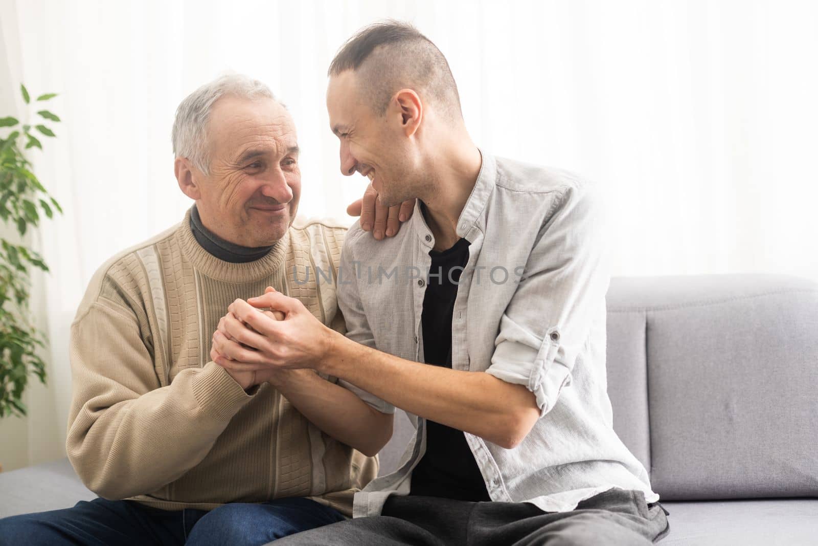 Young adult caucasian son listening and supporting his old elderly senior father at home indoors. Care and love concept. by Andelov13