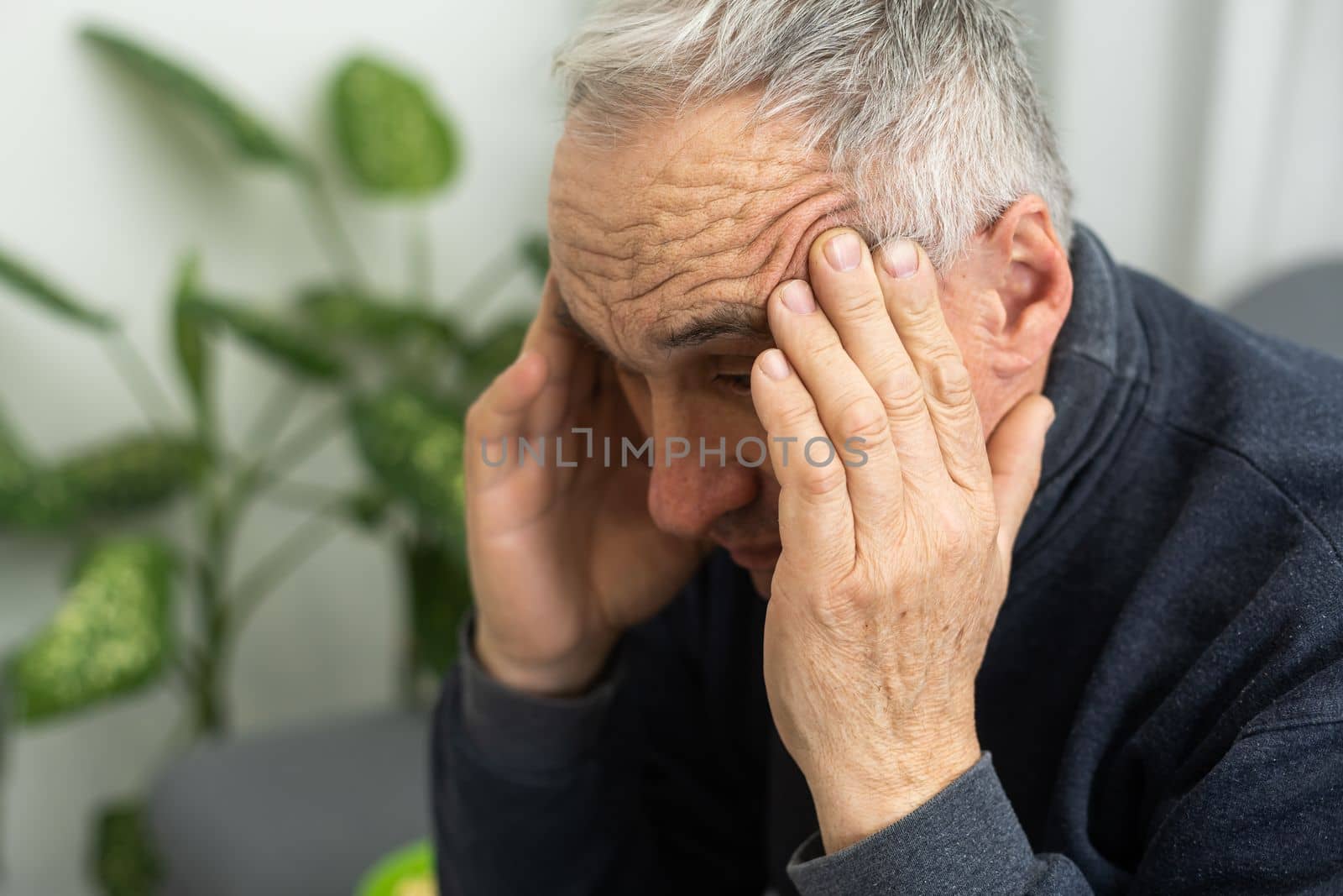 Tired old man suffering from headache, massaging his temples. Strong migraine attack. An elderly man has a headache, massaging his temples.