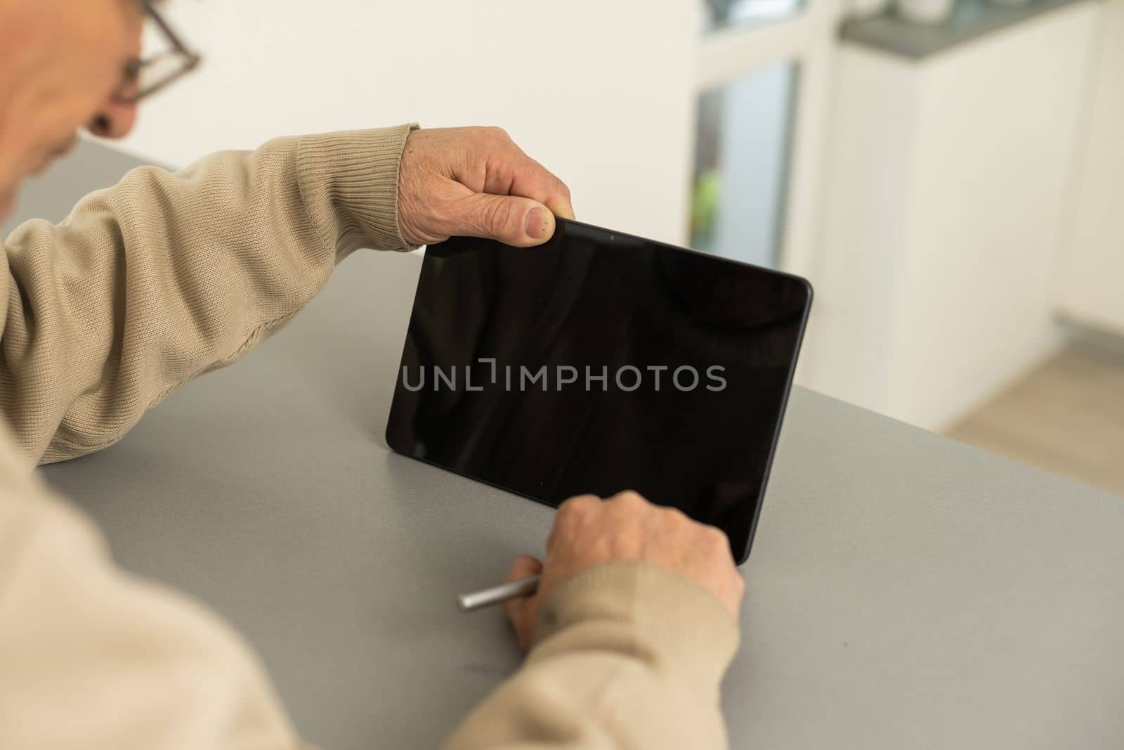 Senior man reading news on digital tablet. Serious mature male using portable computer at home, sitting at table, copy space